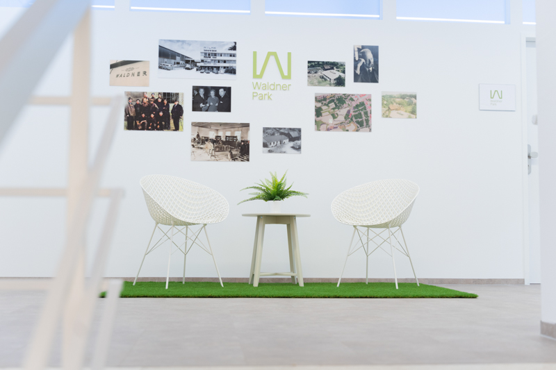 Empfangsbereich mit zwei weißen Stühlen, Tisch und einer Wand mit historischen Fotos