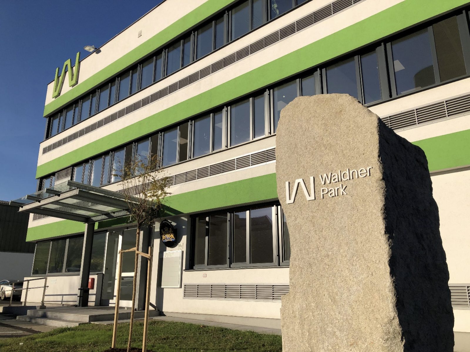 Bürohaus 1 mit grünen Fassadenbändern und Granitstele im Waldner Park